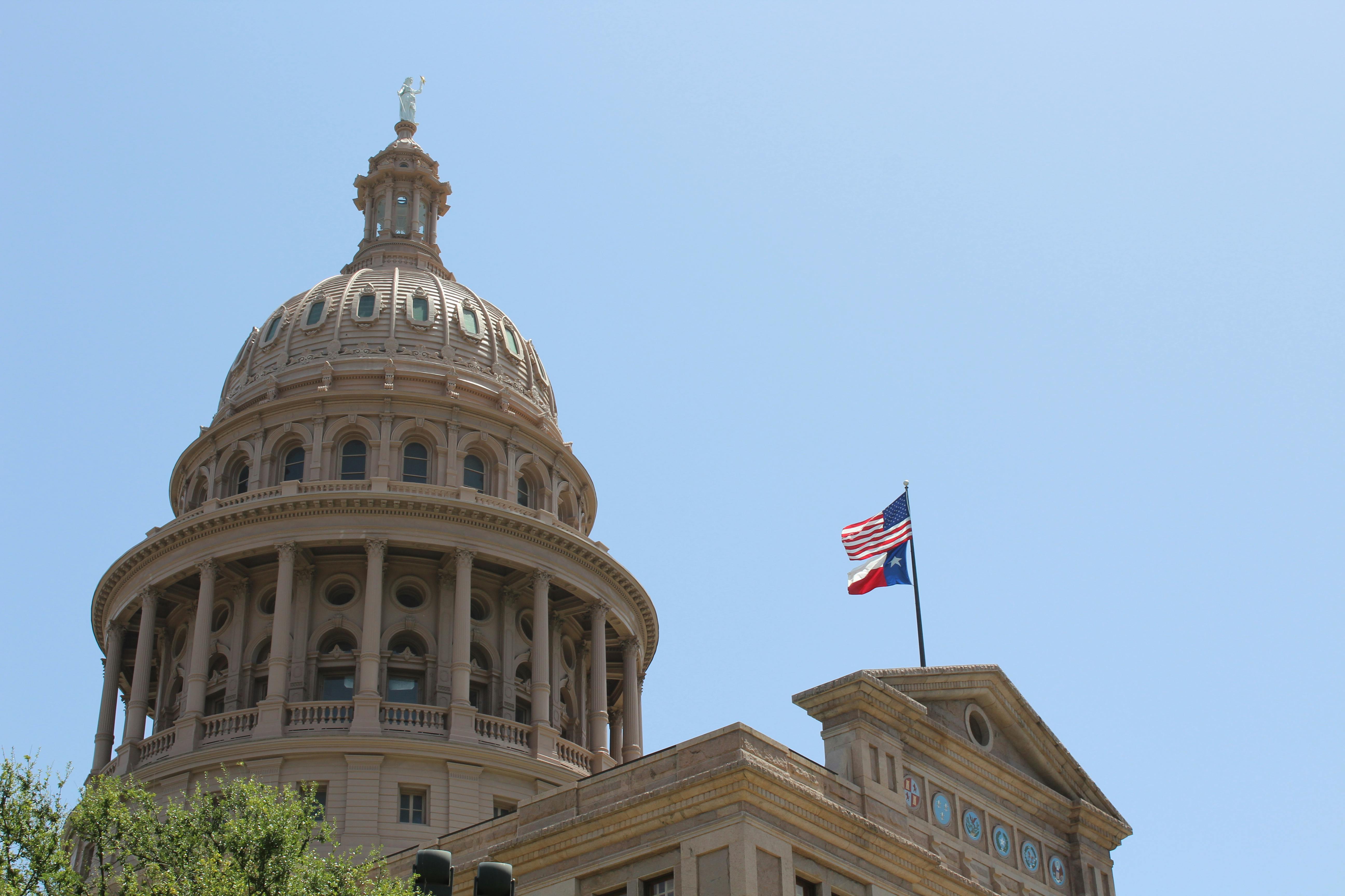 The Texas State Capitol dome with the American and Texas flags flying against a clear blue sky